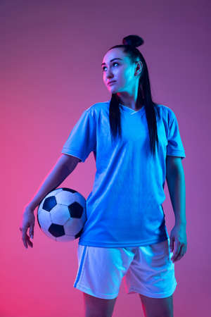 Portrait of beautiful girl, professional female soccer player posing with football ball isolated on purple studio background in neon light. Sport, team, games, fitnessの写真素材