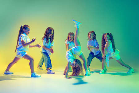 Group of children, little girls in sportive casual style clothes dancing in choreography class isolated on green background in yellow neon light. Concept of music, fashion, artの写真素材