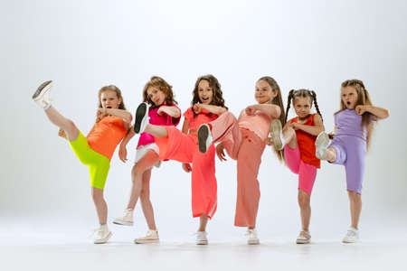 Dance group of happy, active little girls in bright colorful clothes dancing isolated on white studio background. Concept of music, fashion, art, childhood, hobbyの写真素材