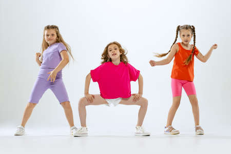 Three little girls, kids in bright colorful clothes dancing, posing isolated on white studio background. Concept of music, fashion, art, childhood, hobbyの写真素材