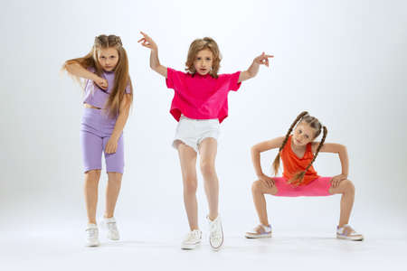 Portrait of happy, active little girls, happy kids in bright colorful clothes dancing isolated on white studio background. Concept of music, fashion, art, childhood, hobbyの写真素材