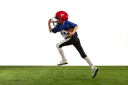 Dynamic portrait of little boy, beginner player of american football training isolated on white background with green grass flooring. Concept of sport, movement, achievements.の写真素材