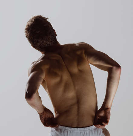Back view of young shirtless muscled man wearing white boxer-briefs standing isolated on gray...