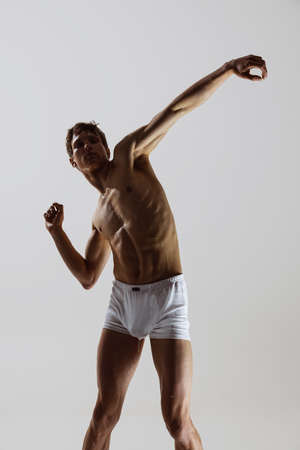 Contemp dance, performance. Young flexible shirtless man in underwear dancing isolated on gray background. Art, music, beauty. Healthy lifestyle conceptの写真素材