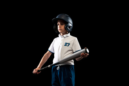 One kid, little baseball player in blue-white uniform leaning to play baseball isolated on black studio background. Concept of sport, achievements, studying, competitionの写真素材