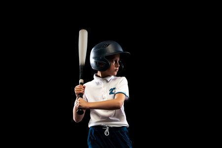 Dynamic portrait of little baseball player, pitcher in blue-white uniform training isolated on black studio background. Concept of sport, achievements, studying, competitionの写真素材