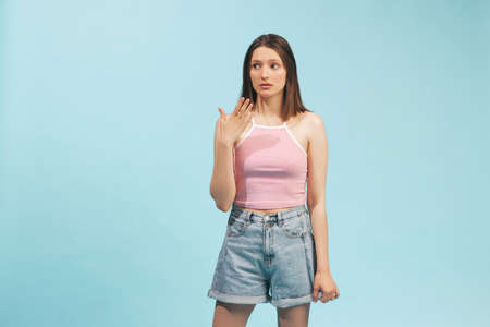 Portrait of emotional girl wearing top and denim shorts posing isolated on blue background. Concept...
