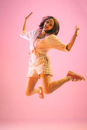 Cheerful young pretty girl in summer fashion collection outfit jumping isolated on pink background....
