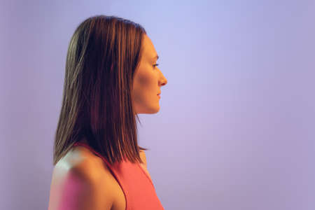Profile view of young beautiful girl with a bob haircut isolated on blue background in neon light. Concept of emotions, facial expression, youthの写真素材