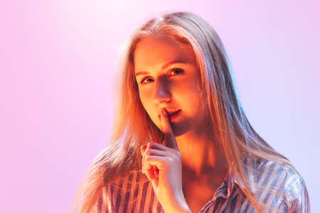 One young beautiful girl, student with long blond hair looking at camera isolated on pink background...