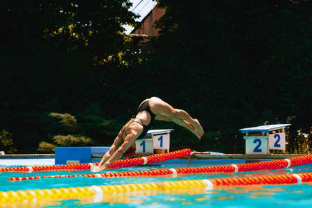 Sportive woman, swimmer jumping to pool, outdoors. Vacation, active lifestyle, power, energy, sports movement concept.の写真素材
