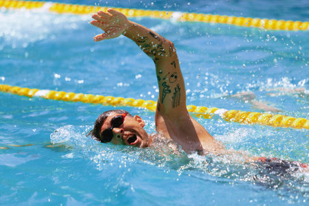 Young muscular man, professional swimmer in goggles training at public swimming-pool, outdoors. Sport, power, energy, style, hobby concept.の写真素材