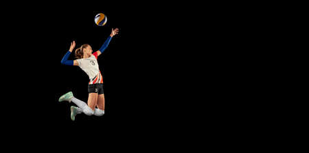 Dynamic portrait of professional volleyball player in sports uniform playing volleyball isolated on dark background. Sport, healthy lifestyle, team, action, motion conceptの写真素材