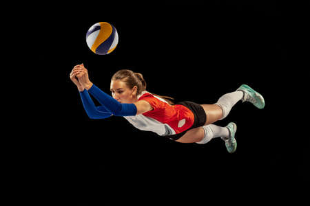 Dynamic portrait of professional volleyball player in sports uniform playing volleyball isolated on dark background. Sport, healthy lifestyle, team, action, motion conceptの写真素材