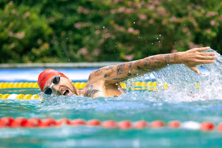 Live portrait of young sportive man, professional swimmer in goggles training at public...