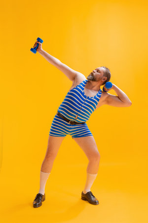 Cute fat young man wearing retro striped swimsuit doing sport exercises isolated on bright yellow background. Sport, vacation, summer, humorの写真素材