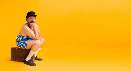One funny beachgoer, fat excited man wearing retro striped swimsuit and vintage bowler hat holding...