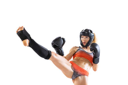 Dynamic portrait of young female kickboxer in sports uniform and protective equipment training isolated on white background. Combat sport, mma, concept.の写真素材