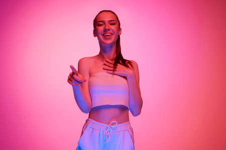 Young beautiful girl with long hair posing isolated on magenta color background in neon light. Concept of beauty, art, fashion, emotions, youthの写真素材