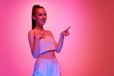 Happy young beautiful girl with long hair posing isolated on magenta color background in neon light. Concept of beauty, art, fashion, emotions, youthの写真素材