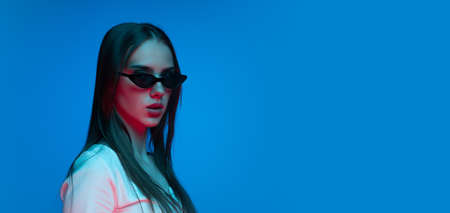 Half-length shot of emotional girl with long glossy dark hair isolated on blue background in neon...