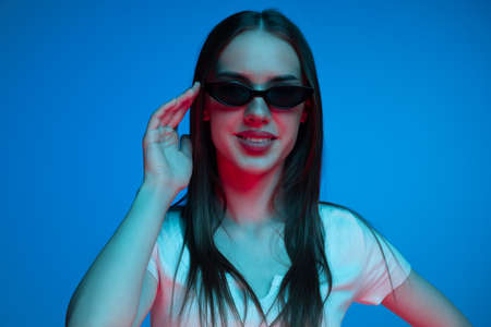 Half-length shot of emotional girl with long glossy dark hair isolated on blue background in neon...