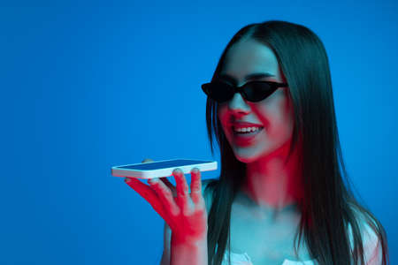 Half-length shot of emotional girl with long glossy dark hair isolated on blue background in neon...