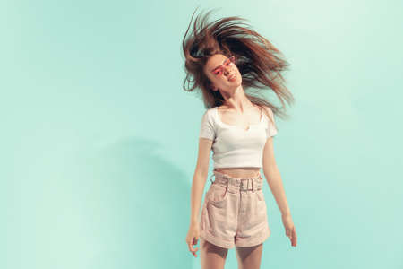 Excited young beautiful girl with long hair posing isolated on light blue color background. Concept of beauty, art, fashion, emotions, youthの写真素材