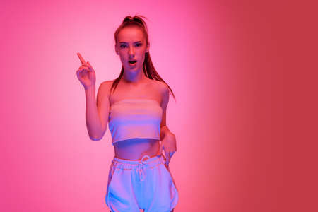 Young beautiful girl with long hair posing isolated on magenta color background in neon light....