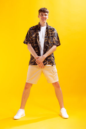 Emotional young man, teen in short and shirt standing isolated on bright yellow studio backgroud. Human emotions, facial expression, summer fashion concept.の写真素材