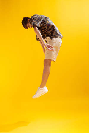 Full-length mans portrait isolated on bright yellow studio backgroud. Young emotional man jumping....