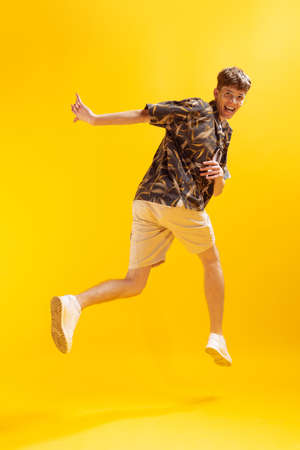 Full-length mans portrait isolated on bright yellow studio backgroud. Young emotional man jumping....