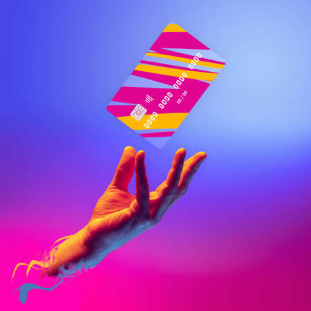 Contemporary art collage. Modern colorful design with male hand and multicolored credit card isolated on gradient blue pink background in neonの写真素材