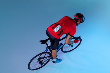 High angle view of professional cyclist in red sports uniform, goggles and a helmet on blue background. Concept of active life, rest, travel, energy, sportの写真素材
