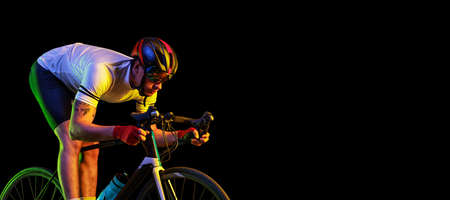 Flyer with male cyclist riding bicycle wearing cycling shorts and protective helmet isolated on dark background in neon. Concept of sport, speed, energyの写真素材