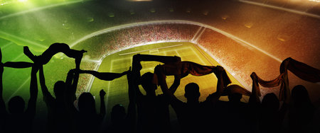 Back view of football, soccer fans cheering their team with scarfs at crowded stadium at evening time. Concept of sport, support, competition. Out of focus effectの写真素材