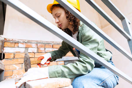 Live portrait of young woman, builder wearing helmet using different work tools at a construction...