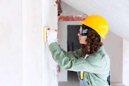 Live portrait of young woman, builder wearing helmet using different work tools at a construction...