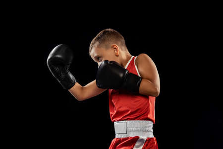 Young beginner boxer, sportive boy training isolated over dark background. Concept of sport,...