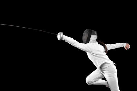 Energetic female fencer in white fencing costume and mask in action, motion isolated on dark...