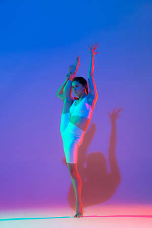 Studio shot of young flexible girl in fitness sport uniform practicing isolated on gradient pink-purple background in neon light. Sport, beauty, adの写真素材