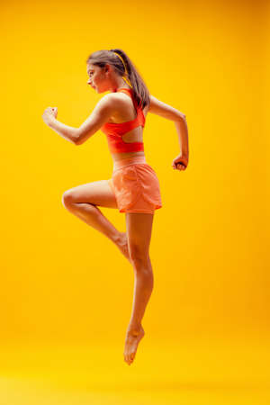 Full-length portrait of young sportive girl in motion isolated on bright yellow background. Modern sport, action, motion, summer, vacation, youth concept.の写真素材