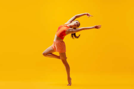 Portrait of young slim, flexible girl in shorts doing stretching exercises isolated on bright yellow background. Sport, health, active lifestyleの写真素材