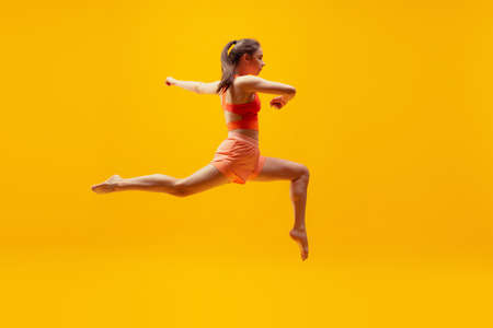 Full-length portrait of young slim girl running isolated on bright yellow background. Modern sport, action, motion, summer, vacation, youth concept.の写真素材
