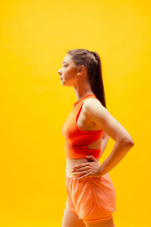 Profile view of young girl wearing summer sports style outfit isolated on bright yellow background. Sport, health, active lifestyleの写真素材