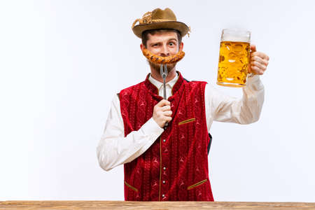 Happy man wearing traditional fest Bavarian or German outfit with big beer glass and fried sausage celebrating Oktoberfest. Party, holiday, ad,sales conceptの写真素材