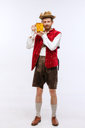 Young expressive man in hat, wearing fest traditional Bavarian or German costume with big beer glass. Alcohol, traditions, holidays, Oktoberfest concept.の写真素材