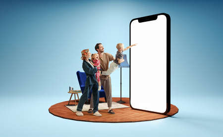 Happy family standing in front of huge 3d model of smartphone with empty white screen isolated on blue background. New app, holiday, travel, ad conceptの写真素材