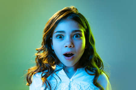 Closeup shocked little girl, kid in casual style clothes isolated over cyan color background in white neon light. Concept of children emotions, fashion, beauty, school and adの写真素材