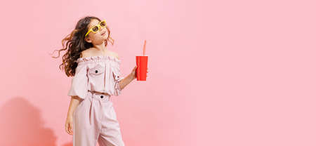 Fashionable little girl, kid posing isolated over pink color background. Concept of children emotions, fashion, happy childhood, beauty, school and adの写真素材